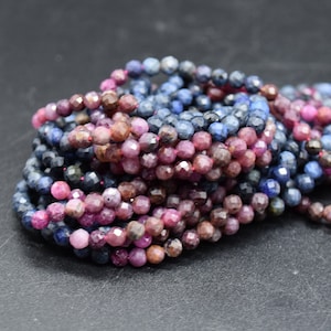 May include: A selection of faceted gemstone beads in shades of blue, pink, and brown. The beads are strung together, creating a textured and colourful display. The gemstones are round and appear to be polished.