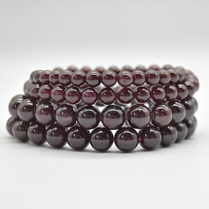 Pode incluir: Um conjunto de quatro pulseiras de pedras preciosas de granada, cada uma com contas redondas, de cor vermelho escuro.
