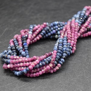 Puede incluir: Múltiples hebras de cuentas facetadas en tonos azul oscuro y magenta. Las cuentas están ensartadas, creando un efecto en capas. Las cuentas tienen una superficie pulida y reflectante, sobre un fondo oscuro.