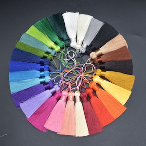 May include: A collection of 20 colorful silk tassels arranged in a circle. The tassels are all the same size and shape, and they are made of a soft, silky material. The tassels are a variety of colors, including red, orange, yellow, green, blue, purple, pink, and white.
