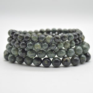 May include: A stack of green and black gemstone bracelets. The beads are round and have a mottled pattern.