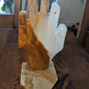 May include: A hand-shaped sculpture made of white and brown onyx. The sculpture is on a white onyx base.
