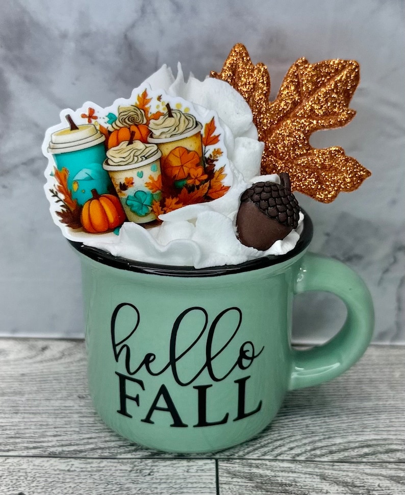 May include: A white ceramic mug with a black handle and the text "But First, Coffee" in a black, bold font. The mug is on a white surface.