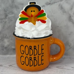 May include: A white ceramic mug with a black handle and the text "But first, coffee" in a handwritten style. The mug is on a white surface. The mug is likely for hot beverages.