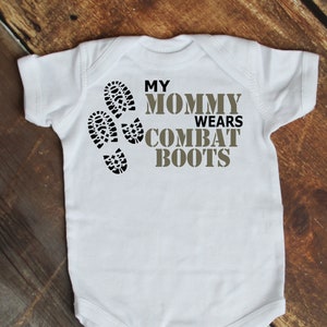 May include: White baby onesie with the text "My Mommy Wears Combat Boots" in brown and black lettering. Three black boot prints are to the left of the text.