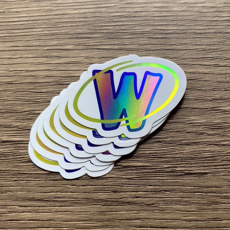 K&ouml;nnte beinhalten: Ein Stapel wei&szlig;er ovaler Aufkleber mit einem holografischen Buchstaben W in einem gelben Kreis. Der Buchstabe W ist schillernd und hat einen blauen Umriss.