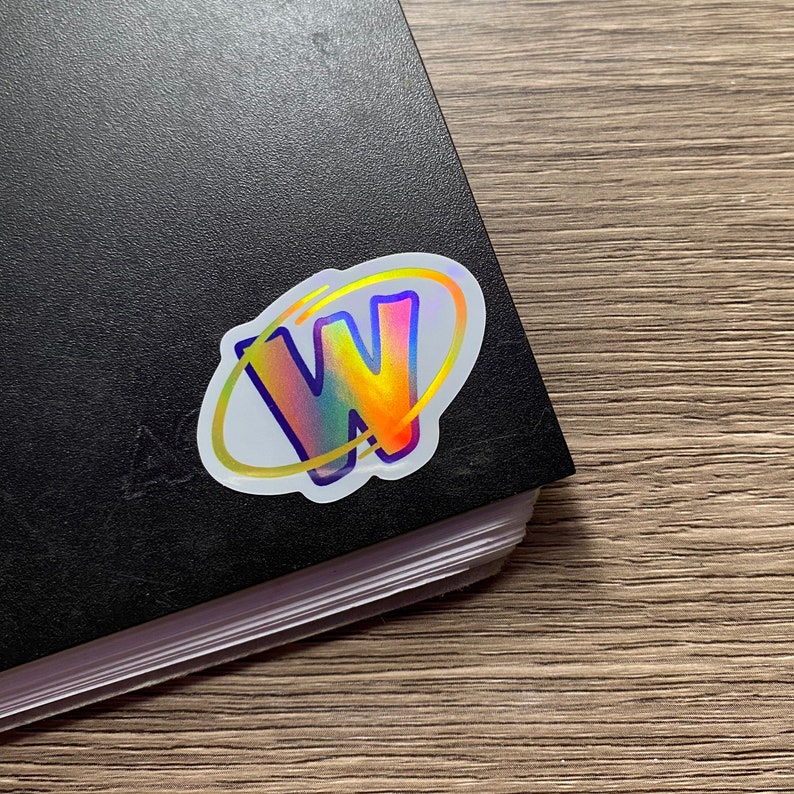 K&ouml;nnte beinhalten: Ein holografischer Aufkleber mit wei&szlig;em Hintergrund und einem gelben, orangefarbenen, roten, blauen und violetten schillernden Buchstaben W in einem gelben Oval.