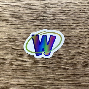 K&ouml;nnte beinhalten: Ein wei&szlig;er Aufkleber mit einem holografischen regenbogenfarbenen Buchstaben "W" in einem gelben Kreis.