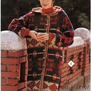 Pode incluir: Um casaco de crochê com capuz e um padrão geométrico em tons de marrom, vermelho, preto e branco. O casaco tem fecho de botão e é mostrado sendo usado por uma pessoa.