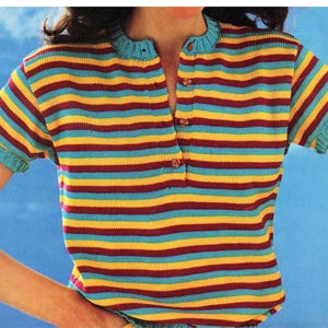 May include: A short-sleeved, striped shirt in a retro style. The shirt features horizontal stripes in teal, yellow, and maroon. It has a button-up neckline and teal trim on the sleeves and collar. The shirt is made of a knitted material.
