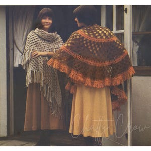 May include: Two women wearing crocheted shawls. One shawl is brown and orange with a fringe, the other is cream with a fringe. Both women are wearing brown skirts.