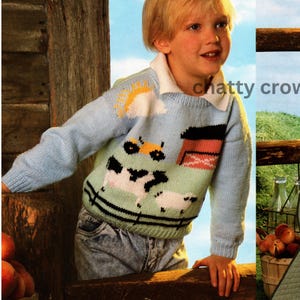May include: A light blue knitted jumper with a farm scene design. The jumper features a sun, clouds, cows, a tractor, and a red barn. The jumper has a white collar and is worn by a young child.