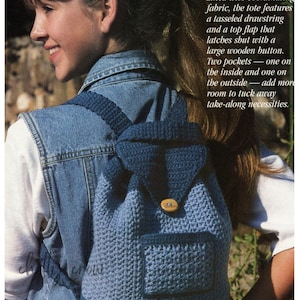 May include: A blue crocheted backpack with a wooden button closure and two pockets. The backpack is being worn by a person wearing a denim vest.