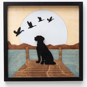 May include: A black silhouette of a dog sitting on a wooden jetty overlooking a body of water. The background features a large white circle with four black silhouettes of geese flying in formation.