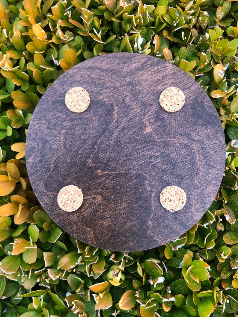May include: A dark brown round wooden coaster with four cork circles attached to the bottom.
