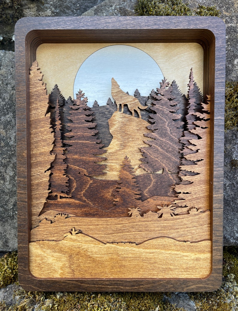 May include: A wooden wall art piece depicting a wolf howling at the moon in a forest setting. The wolf is silhouetted against a light blue moon, and the trees are carved in a layered style, creating a 3D effect.