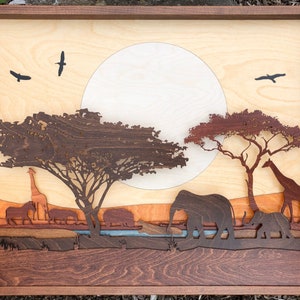 May include: A wooden wall art piece depicting a safari scene with a large moon, two trees, a giraffe, elephants, and birds. The art piece is made of different shades of wood and has a layered effect.