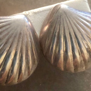 May include: A pair of silver shell-shaped earrings. The earrings are made of smooth, shiny metal and have a detailed, ribbed texture.