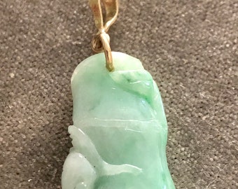 May include: A green jade pendant with a gold bail. The jade is carved into a figure of a person.