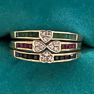 May include: Three gold rings with a clover design set with diamonds. The rings are stacked with emerald green, ruby red, and sapphire blue stones.