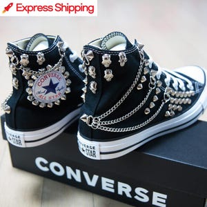 May include: Black high-top Converse sneakers customized with silver skull and spike studs, and chain accents. The sneakers feature the Converse All Star logo and are displayed on a black Converse box.