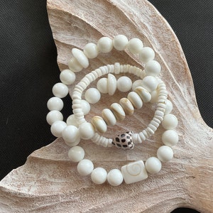 May include: Three white shell bead bracelets with a brown and white shell charm and a white shell square charm.