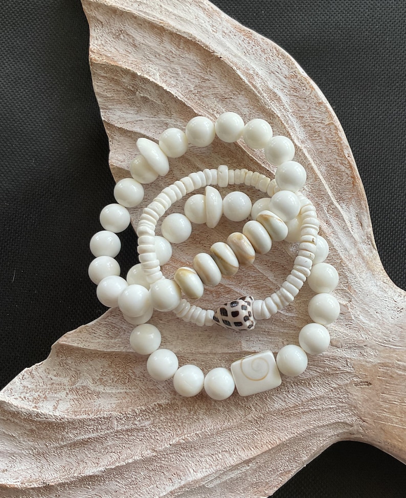 May include: Three white shell bead bracelets with a brown and white shell charm and a white shell square charm.