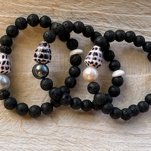 May include: Three black lava rock bracelets with white and pink shell beads and pearl accents.