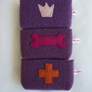 May include: Three purple felt pouches with different felt appliques. The top pouch has a pink crown, the middle pouch has a pink bone, and the bottom pouch has an orange cross. Each pouch has a white label with the word "Heinz" on it.