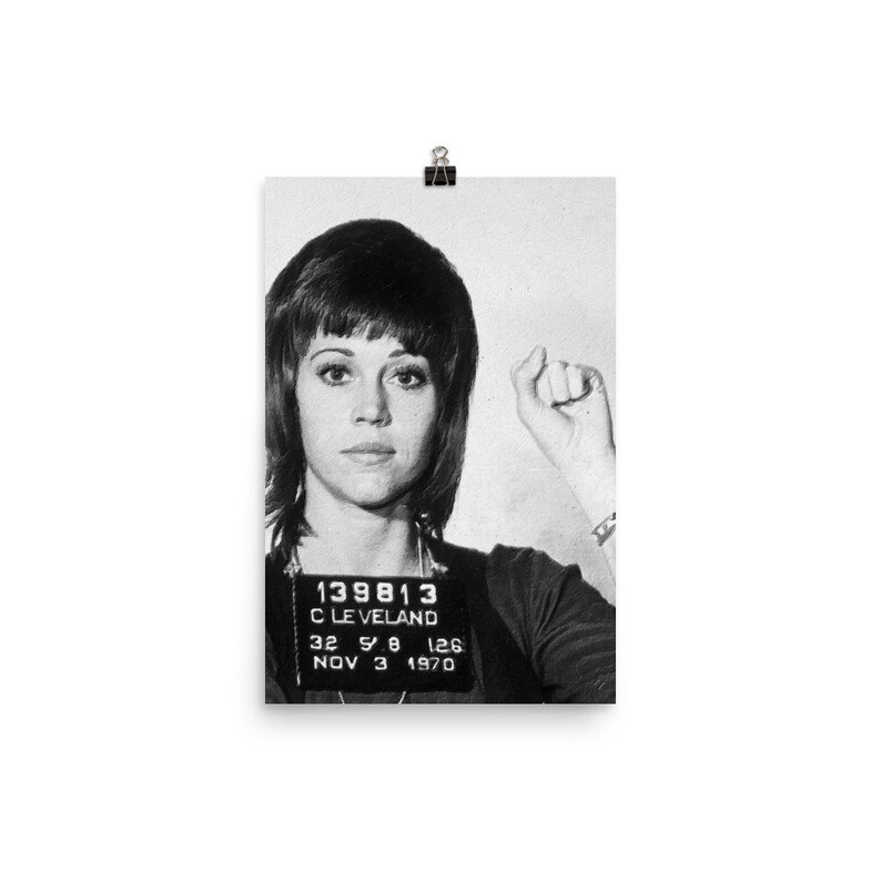 May include: Black and white mugshot style photo of a woman with short dark hair. The photo includes a police booking card with the text "139813 CLEVELAND 32 5 8 126 NOV 3 1970".