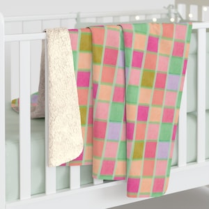 Op de afbeelding: Een zachte, pluche deken met een geruit patroon in tinten roze, groen en oranje. De deken is gemaakt van een zacht, comfortabel materiaal en is perfect om te knuffelen op de bank of in bed.