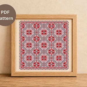May include: A framed cross-stitch pattern featuring a repeating floral design in red, black, and white. The pattern is set against a beige background and enclosed in a light brown wooden frame. The text "PDF Pattern" is in a brown circle.
