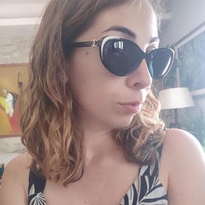 Puede incluir: Gafas de sol negras de gran tama&ntilde;o con un acento blanco en la parte superior de la montura. Las gafas de sol tienen lentes oscuras y un logotipo dorado en las patillas. La montura es de color marr&oacute;n oscuro. Las gafas de sol las lleva una persona.
