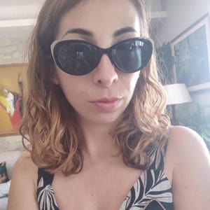 Puede incluir: Gafas de sol negras de ojo de gato con un acento plateado en la parte superior de la montura. La persona lleva una camiseta con estampado en blanco y negro. La persona tiene el pelo ondulado casta&ntilde;o claro.