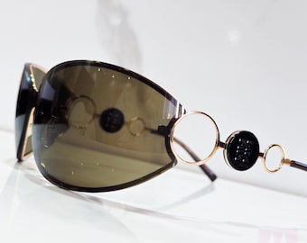 May include: A pair of brown sunglasses with a gold metal frame and black accents. The sunglasses have a unique oval shape and a large, round lens.