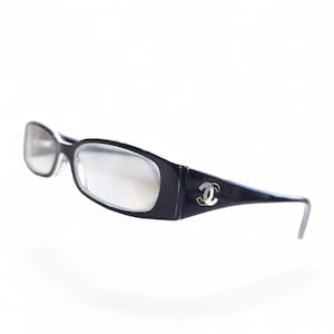 May include: Black rectangular eyeglasses with clear lenses. The frames have a glossy finish and feature a silver-colored logo on the temples. The glasses are designed for vision correction and are suitable for everyday wear.