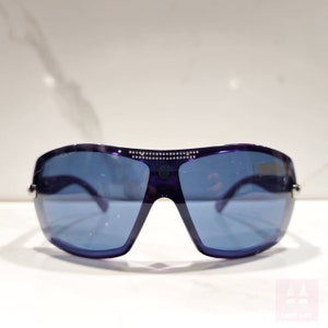 May include: Purple sunglasses with a silver frame and rhinestones on the top. The lenses are blue.