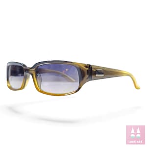 Puede incluir: Gafas de sol rectangulares marrones con lentes azules degradadas. Las gafas tienen una montura rectangular sutil y un pequeño acento plateado en las patillas. Las varillas se curvan hacia las orejeras.