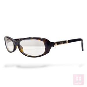 May include: Eyeglasses with a tortoiseshell pattern and a dark brown frame. The temples are black with gold-coloured accents and the brand name. The lenses are clear. The glasses have a slight cat-eye shape.