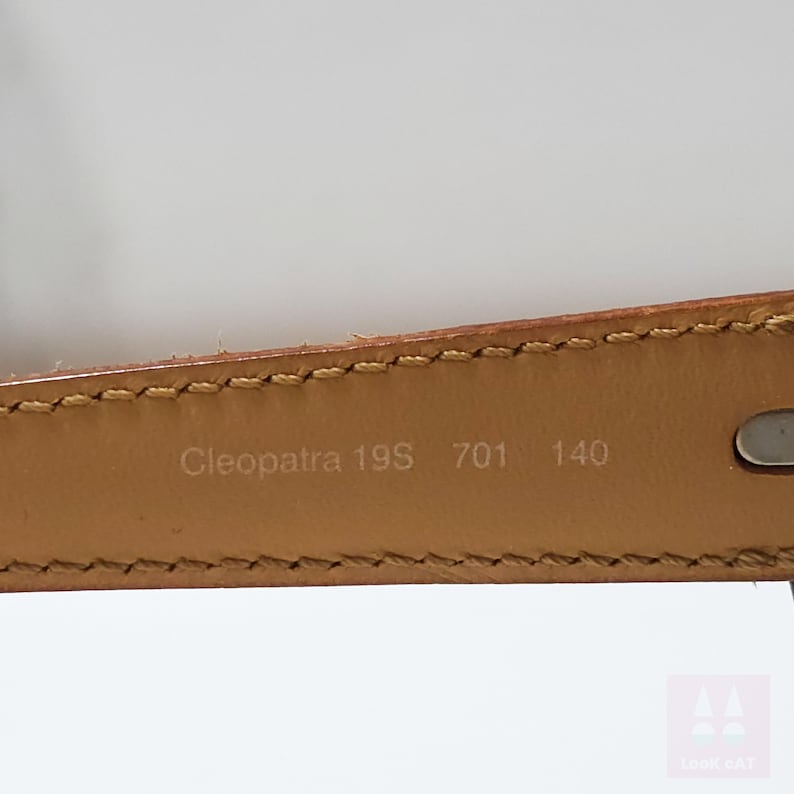 Peut inclure: Gros plan sur une ceinture en cuir marron clair. Le texte "Cleopatra 19S 701 140" est imprim&eacute; &agrave; l'int&eacute;rieur de la ceinture. La ceinture a un bord cousu et une boucle de couleur argent.