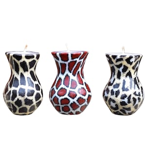 May include: Three decorative candles shaped like vases with animal print designs. The candles are white with black and brown spots, white with red and black spots, and white with black and tan spots.