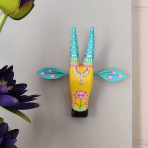 Pode incluir: Cabe&ccedil;a de vaca de madeira pintada &agrave; m&atilde;o, amarela, com chifres turquesa e detalhes rosa e turquesa. A cabe&ccedil;a de vaca apresenta um design floral e &eacute; montada na parede. &Eacute; um objeto decorativo.
