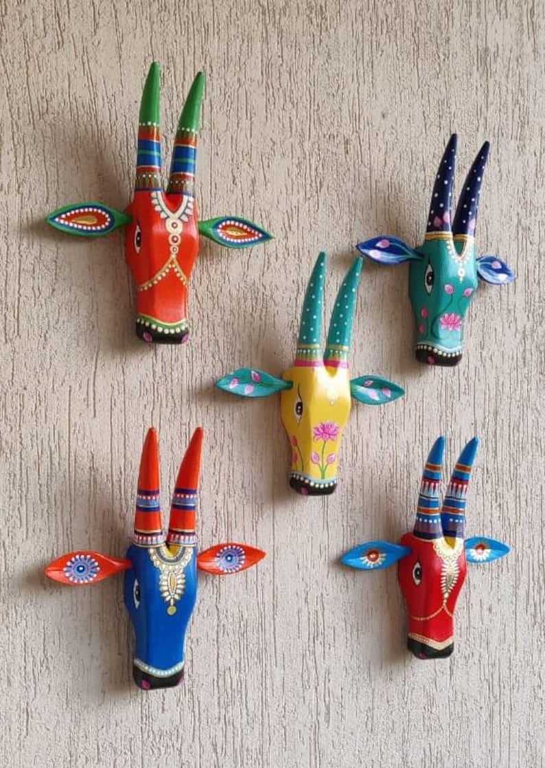 Pode incluir: Cinco penduradores de parede de madeira pintados &agrave; m&atilde;o em forma de cabe&ccedil;a de touro. Cada cabe&ccedil;a apresenta um esquema de cores &uacute;nico, incluindo vermelho, azul, amarelo e turquesa, com padr&otilde;es detalhados nos chifres e orelhas. As pe&ccedil;as decorativas s&atilde;o montadas numa parede texturizada de cor clara.