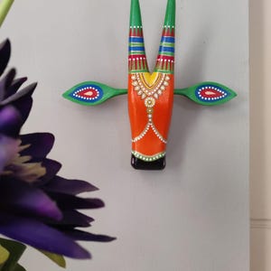 Pode incluir: Uma cabe&ccedil;a de touro de madeira pintada de forma vibrante para pendurar na parede. O touro apresenta um corpo laranja, chifres verdes e detalhes verdes e azuis. O design inclui padr&otilde;es decorativos e uma base preta, criando um estilo de arte popular colorido.