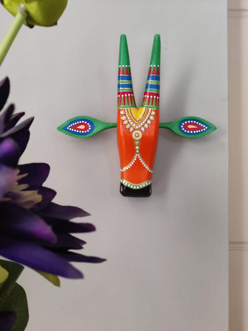 Pode incluir: Uma cabe&ccedil;a de touro de madeira pintada de forma vibrante para pendurar na parede. O touro apresenta um corpo laranja, chifres verdes e detalhes verdes e azuis. O design inclui padr&otilde;es decorativos e uma base preta, criando um estilo de arte popular colorido.