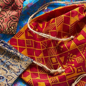 May include: A set of three fabric drawstring bags with different patterns. The bags are made of colorful cotton fabric with geometric and floral designs. The bags are tied with a natural twine cord.