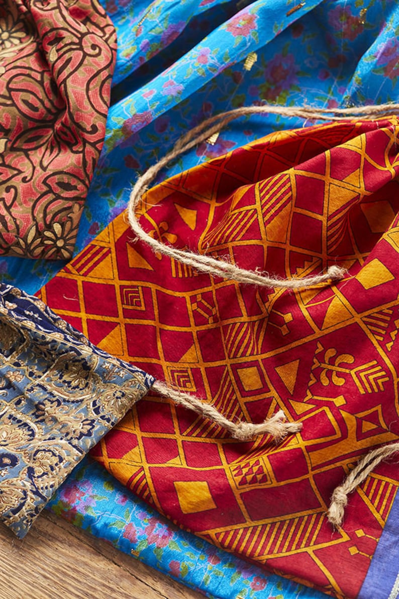May include: A set of three fabric drawstring bags with different patterns. The bags are made of colorful cotton fabric with geometric and floral designs. The bags are tied with a natural twine cord.
