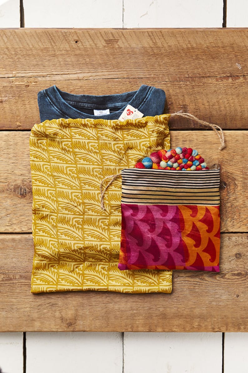 May include: Two fabric drawstring bags, one yellow with a leaf pattern and one with a multi-colored striped top and a pink and orange bottom with a wave pattern. The bags are on a wooden surface.