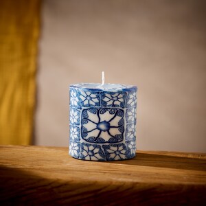 May include: A blue and white patterned candle with a white wick. The candle is cylindrical and has a decorative design.