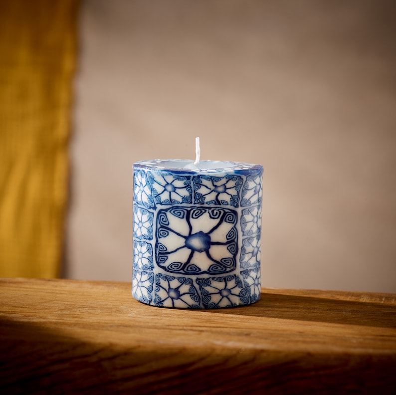 May include: A blue and white patterned candle with a white wick. The candle is cylindrical and has a decorative design.